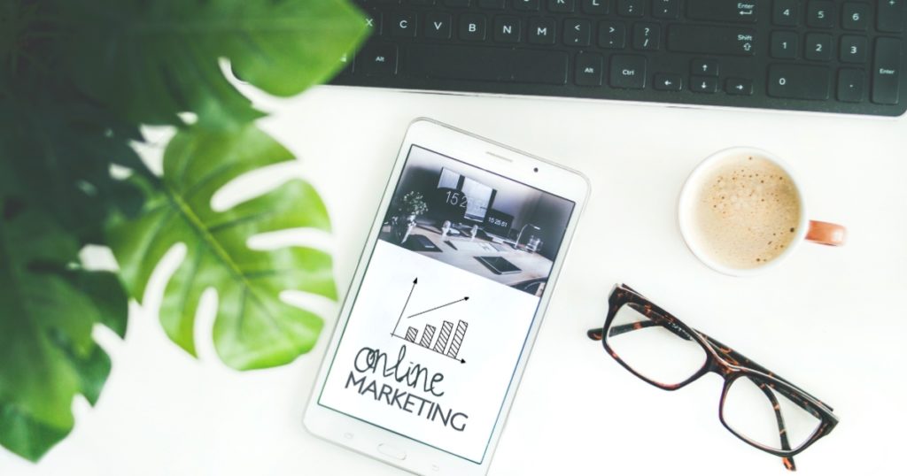 Online Marketing - Desk with phone, pair of glasses, coffee and a plant next to keyboard