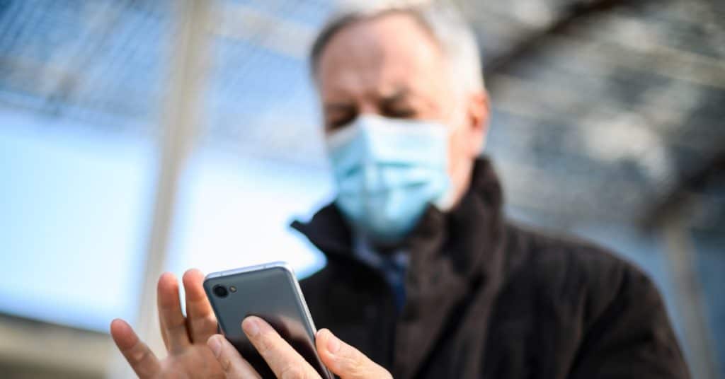 A senior man with mask on looking down at his smartphone