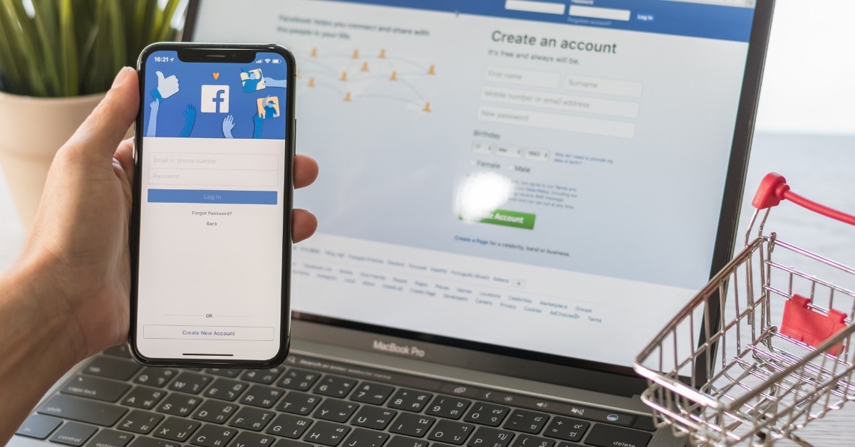 Smartphone & laptop with Facebook open next to plant and shopping cart